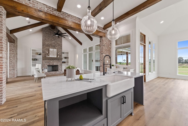 kitchen featuring pendant lighting, a center island with sink, light hardwood / wood-style floors, gray cabinetry, and beamed ceiling