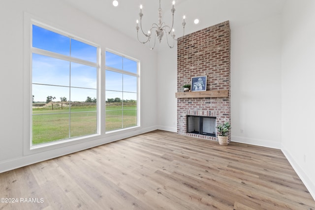 unfurnished living room featuring a brick fireplace, brick wall, a chandelier, and light hardwood / wood-style floors