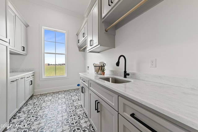 kitchen with light stone counters, white cabinets, light tile patterned floors, ornamental molding, and sink