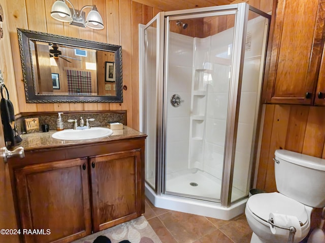 bathroom with toilet, an enclosed shower, vanity, wooden walls, and tile patterned flooring