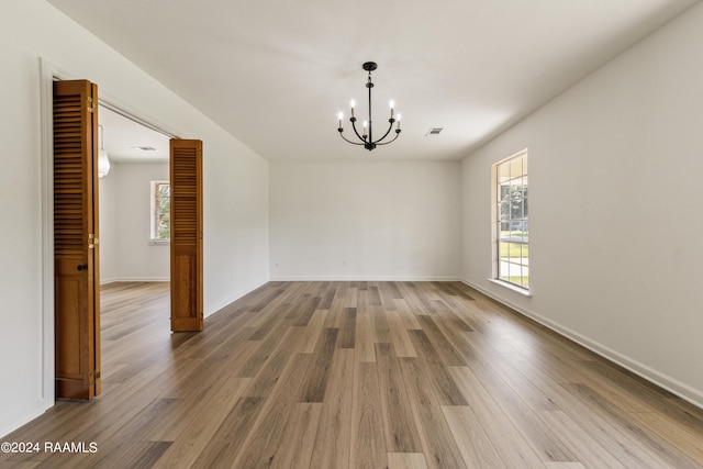 spare room with a healthy amount of sunlight, hardwood / wood-style floors, and a chandelier