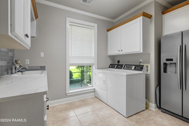 clothes washing area with sink, washing machine and dryer, crown molding, cabinets, and light tile patterned floors