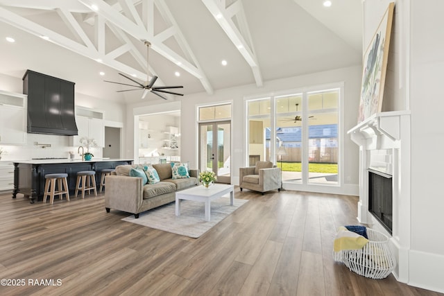 living room with ceiling fan, high vaulted ceiling, hardwood / wood-style floors, beamed ceiling, and sink