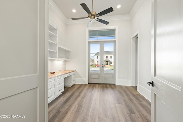 unfurnished office with built in desk, french doors, ceiling fan, crown molding, and light wood-type flooring