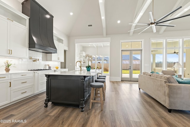 kitchen with a breakfast bar, custom exhaust hood, white cabinets, a kitchen island with sink, and decorative backsplash