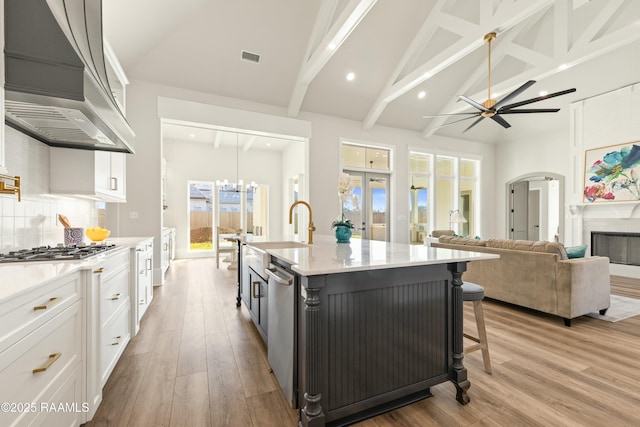 kitchen with a center island with sink, white cabinets, decorative backsplash, and premium range hood