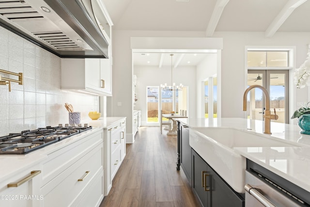 kitchen featuring dishwashing machine, wall chimney range hood, white cabinets, and pendant lighting