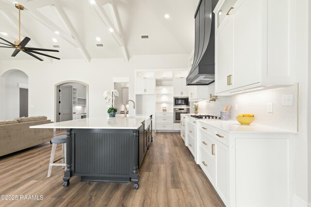 kitchen with appliances with stainless steel finishes, premium range hood, white cabinetry, lofted ceiling with beams, and a large island