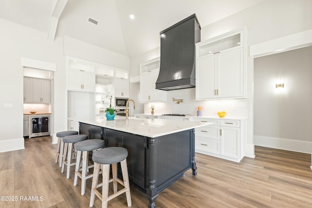 kitchen featuring premium range hood, white cabinetry, a kitchen island with sink, and stainless steel microwave