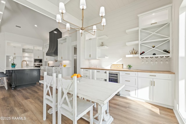 kitchen featuring white cabinets, wooden counters, pendant lighting, and a kitchen island with sink