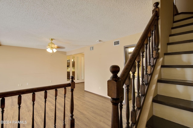 staircase with a textured ceiling, ceiling fan, wood finished floors, and visible vents