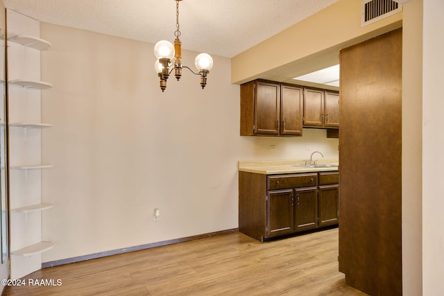 kitchen with sink, a notable chandelier, light wood-type flooring, a textured ceiling, and pendant lighting