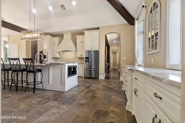 kitchen with visible vents, custom range hood, appliances with stainless steel finishes, hanging light fixtures, and a kitchen bar