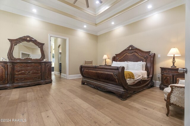 bedroom with light wood-type flooring, crown molding, and a tray ceiling