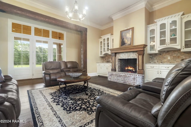 living room featuring dark wood-style floors, a brick fireplace, an inviting chandelier, and crown molding