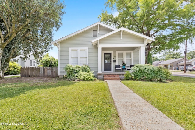 bungalow-style home featuring covered porch, a front lawn, and fence