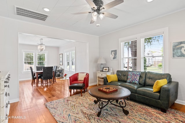 living area with baseboards, light wood finished floors, visible vents, and crown molding