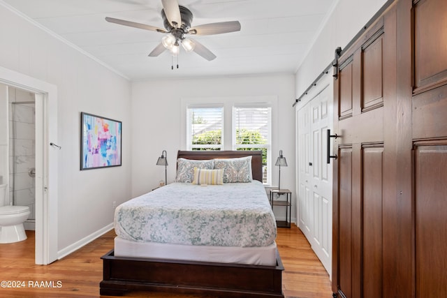 bedroom featuring a barn door, baseboards, light wood-type flooring, ensuite bath, and crown molding