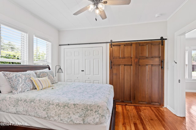 bedroom with a barn door, baseboards, a ceiling fan, ornamental molding, and wood finished floors