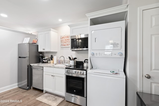 kitchen with white cabinets, light wood-style floors, appliances with stainless steel finishes, crown molding, and stacked washing maching and dryer