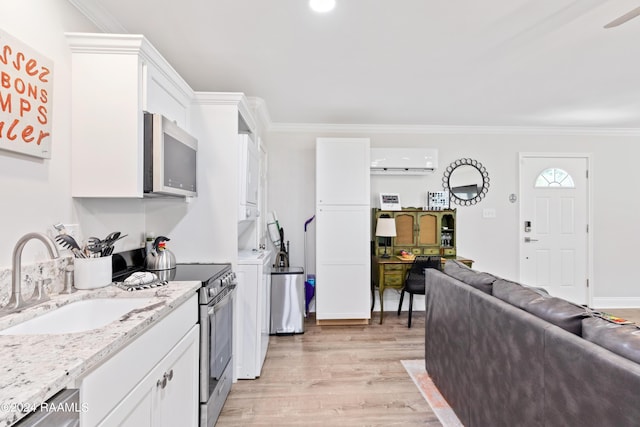 kitchen with stainless steel appliances, stacked washing maching and dryer, a sink, and white cabinetry