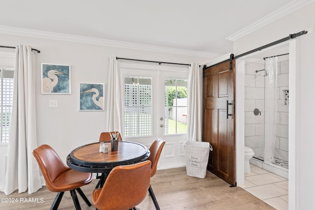 dining room with ornamental molding, a barn door, and light wood-style floors