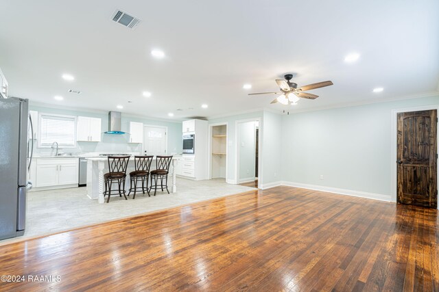 unfurnished living room featuring light hardwood / wood-style floors, ornamental molding, sink, and ceiling fan