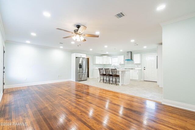 unfurnished living room featuring light hardwood / wood-style flooring, ornamental molding, sink, and ceiling fan