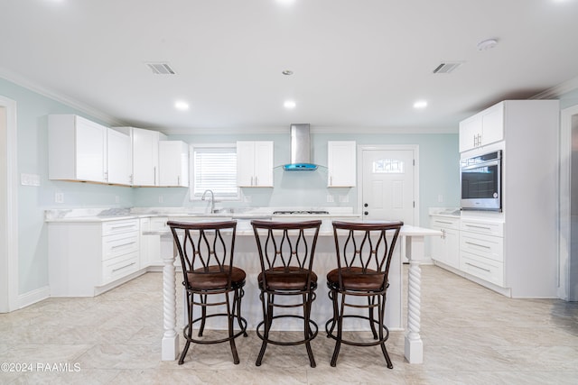 kitchen featuring a kitchen island, wall chimney range hood, crown molding, white cabinetry, and appliances with stainless steel finishes