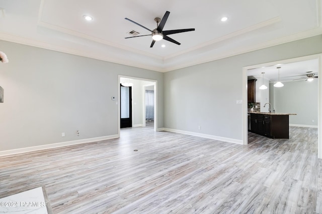 unfurnished living room featuring ceiling fan, sink, light hardwood / wood-style flooring, and a tray ceiling