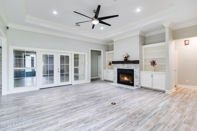 unfurnished living room featuring ornamental molding, a raised ceiling, light wood-type flooring, a fireplace, and ceiling fan