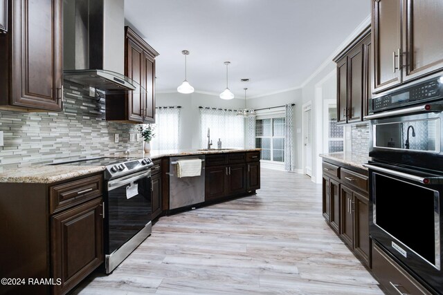 kitchen featuring light wood-type flooring, wall chimney exhaust hood, tasteful backsplash, appliances with stainless steel finishes, and decorative light fixtures