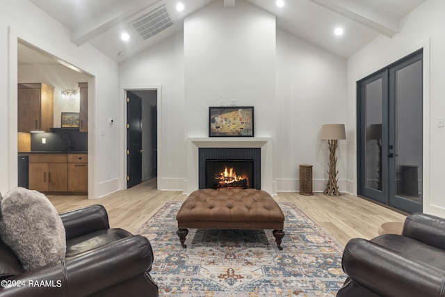 living room with high vaulted ceiling, light wood-type flooring, beam ceiling, and a tile fireplace