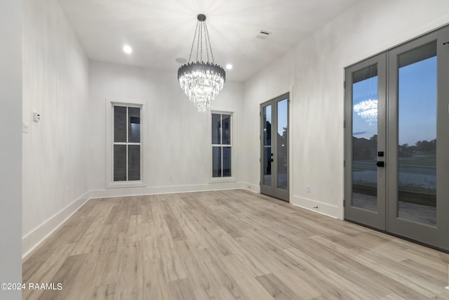 spare room featuring a notable chandelier, light wood-type flooring, and french doors