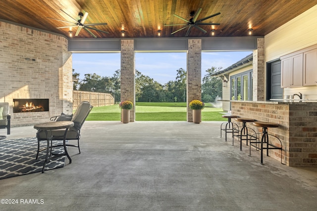 view of patio featuring an outdoor brick fireplace, a wet bar, and ceiling fan