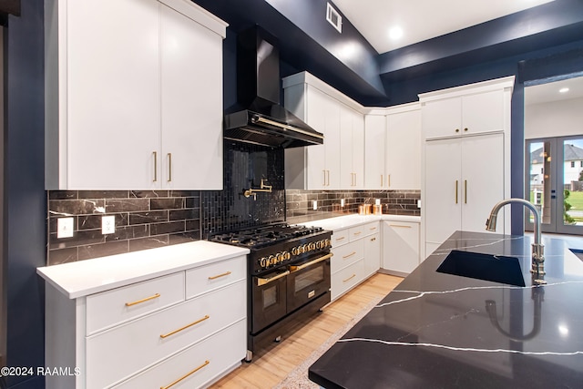 kitchen featuring light hardwood / wood-style floors, white cabinetry, double oven range, sink, and wall chimney range hood