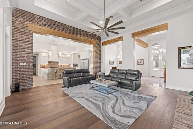 living room featuring coffered ceiling, hardwood / wood-style floors, ceiling fan with notable chandelier, ornamental molding, and beam ceiling