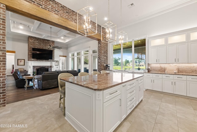 kitchen with a kitchen island, ceiling fan with notable chandelier, light stone countertops, decorative light fixtures, and a brick fireplace