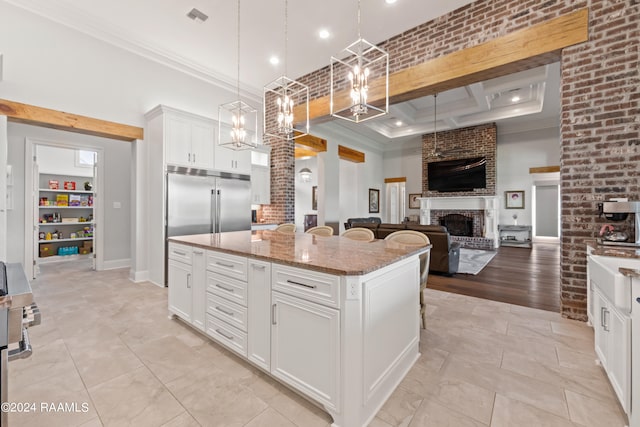 kitchen featuring a fireplace, crown molding, decorative light fixtures, light stone counters, and a center island