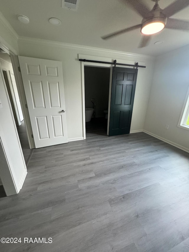 unfurnished bedroom featuring crown molding, ceiling fan, wood-type flooring, and a barn door