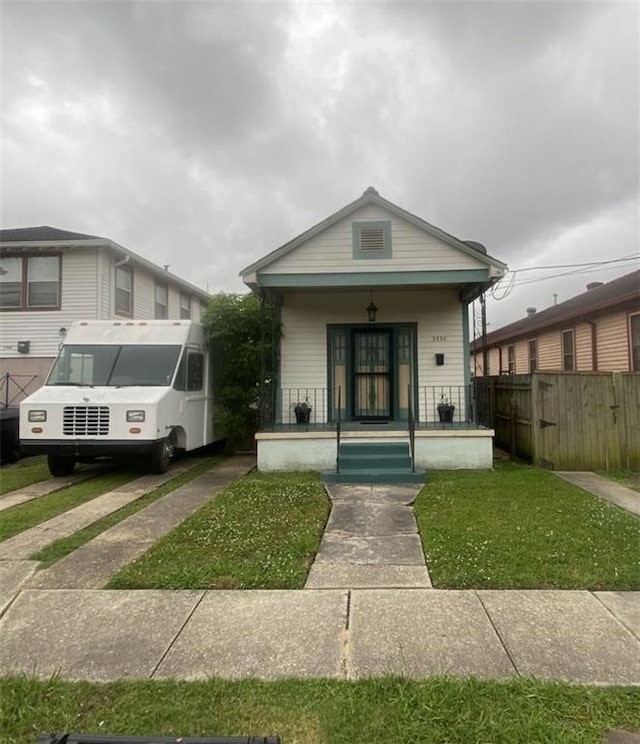 shotgun-style home featuring covered porch and fence