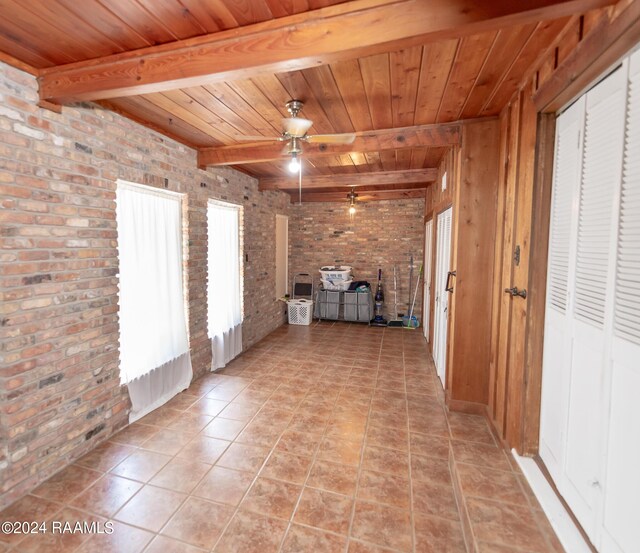 tiled empty room featuring ceiling fan, beam ceiling, wood ceiling, and brick wall