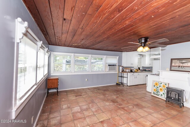 unfurnished living room featuring ceiling fan, wood ceiling, a wood stove, and tile patterned flooring