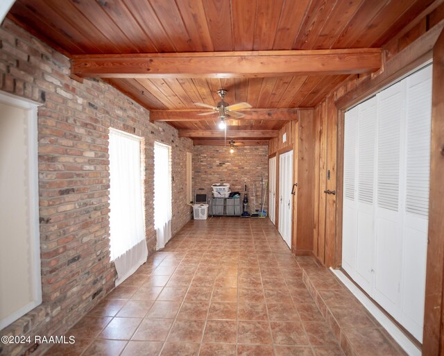 interior space featuring beamed ceiling, light tile patterned floors, brick wall, and wood ceiling