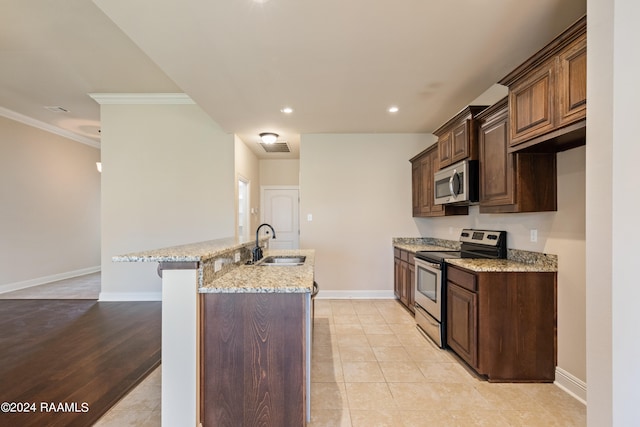 kitchen featuring stainless steel appliances, sink, crown molding, an island with sink, and light wood-type flooring