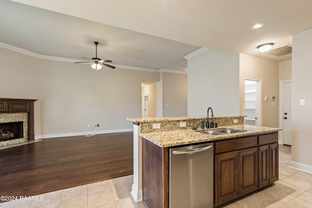 kitchen with sink, a fireplace, an island with sink, dishwasher, and light tile patterned floors