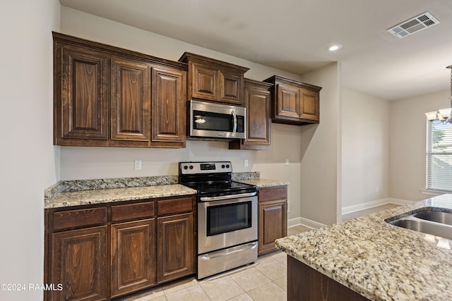 kitchen featuring appliances with stainless steel finishes, a chandelier, dark brown cabinetry, light stone countertops, and light tile patterned flooring