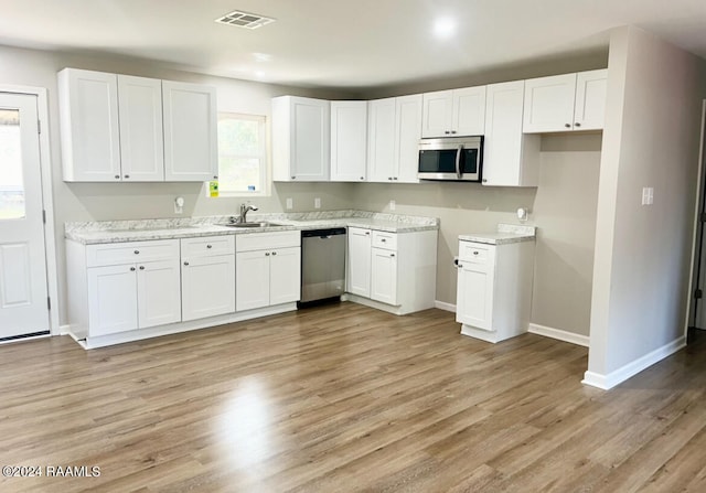 kitchen with light wood-type flooring, appliances with stainless steel finishes, sink, and white cabinetry