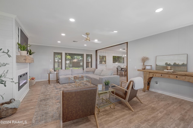 living room featuring ceiling fan, ornamental molding, a fireplace, and light hardwood / wood-style flooring