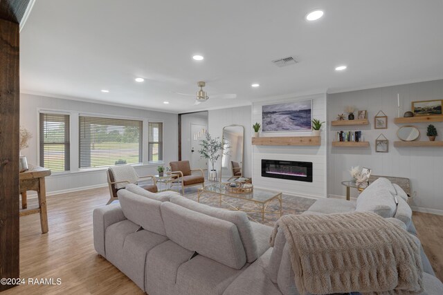 living room with a fireplace, light wood-type flooring, ceiling fan, and crown molding